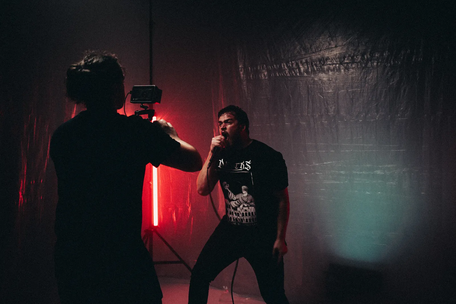 Behind-the-scenes photo of a camera operator filming a vocalist in a dark studio.