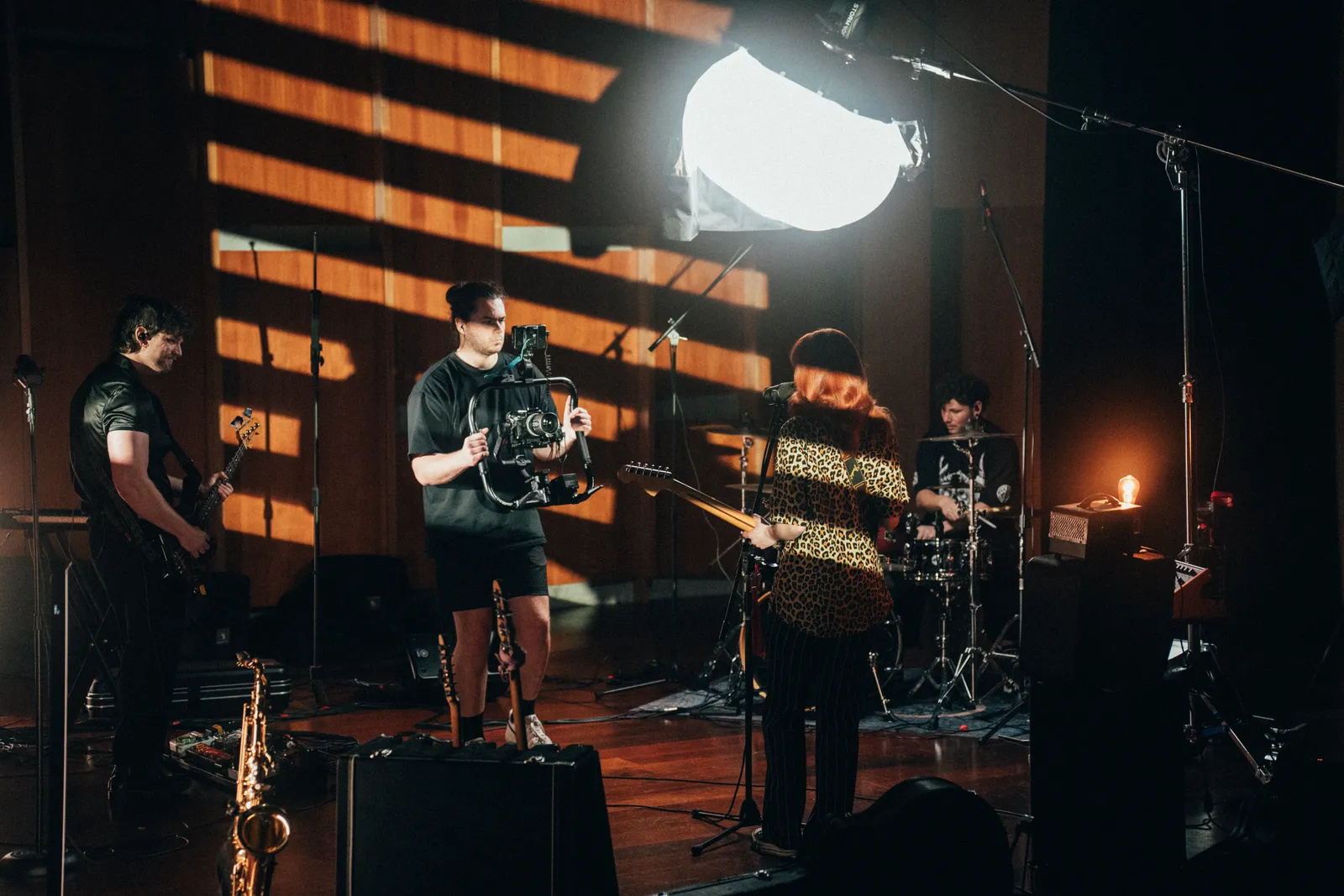 Behind-the-scenes photo of a camera operator with a gimbal rig moving through a band set in a wood-panelled studio.