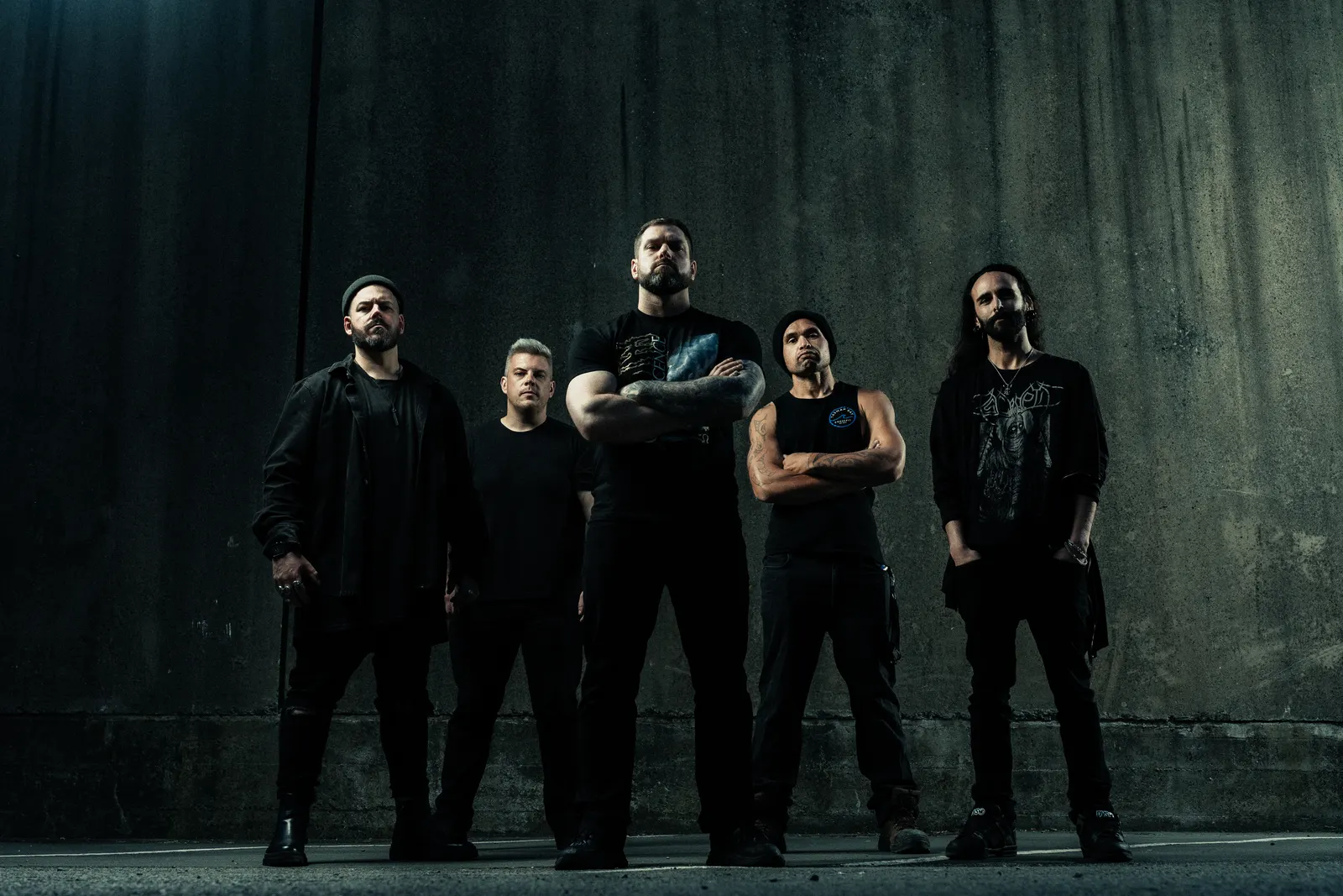Music photography of a band standing against an industrial wall.