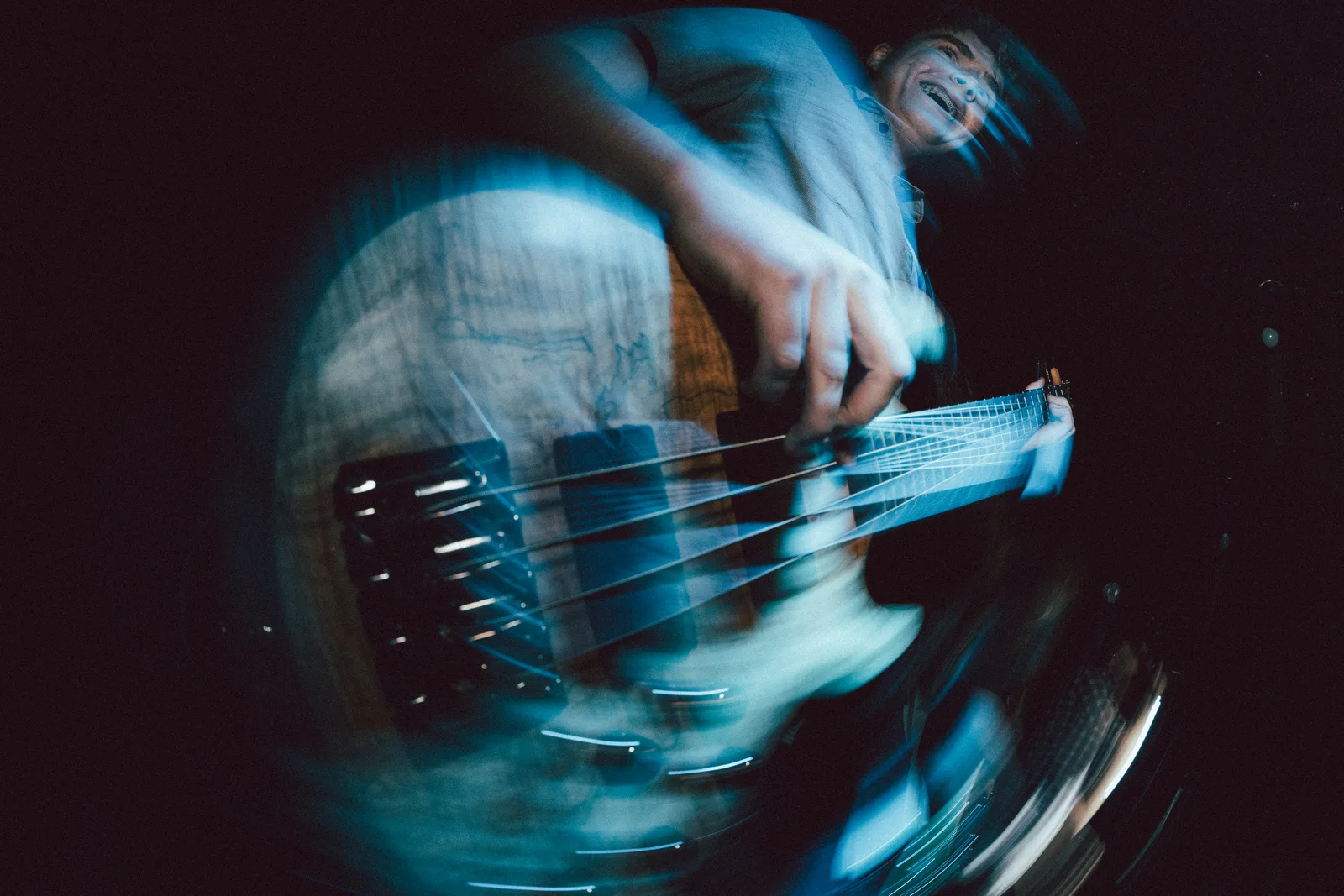 Live music photo of a bassist with radial motion blur under blue light.