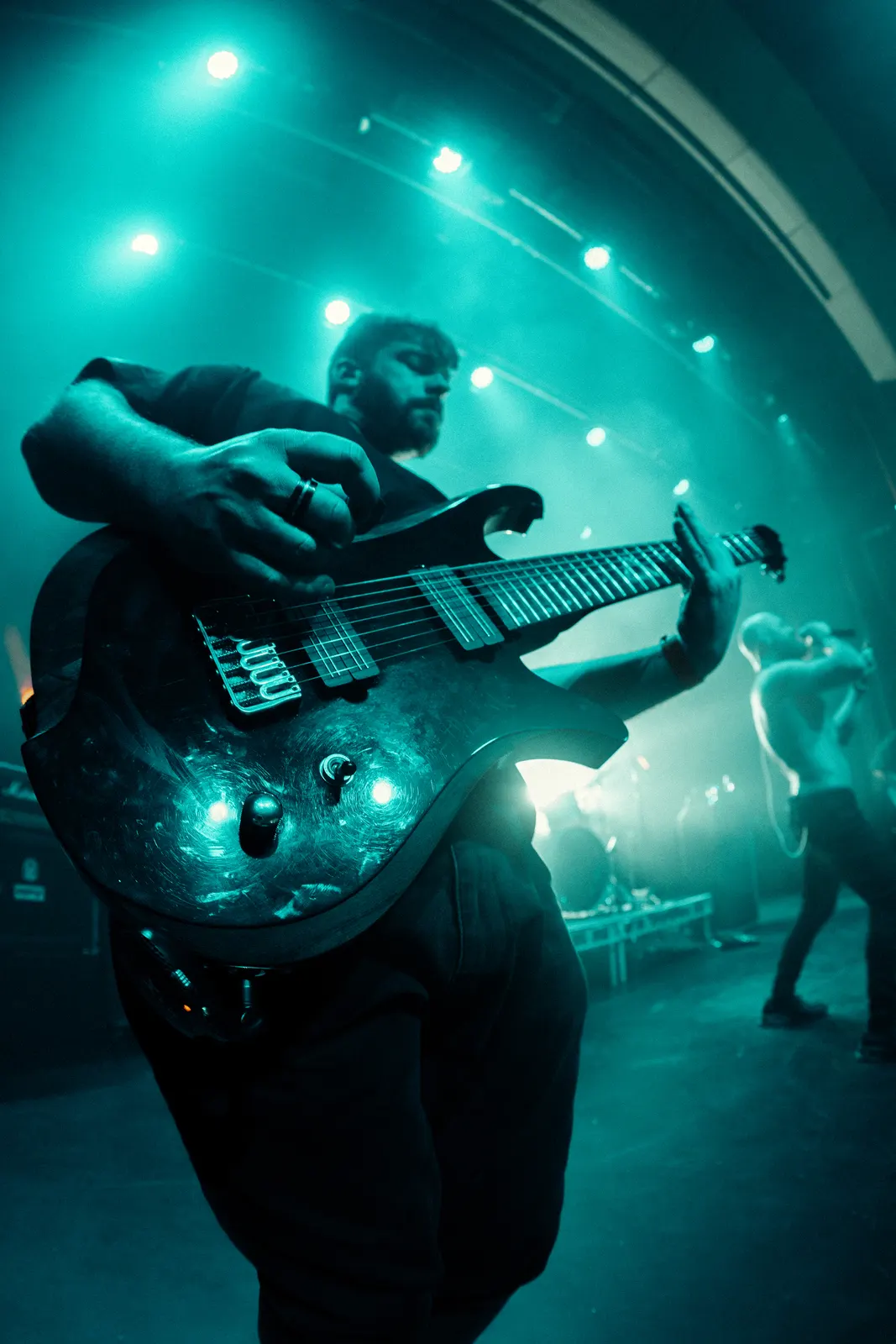 Portrait-orientation live music photo of a bassist under stage lighting.