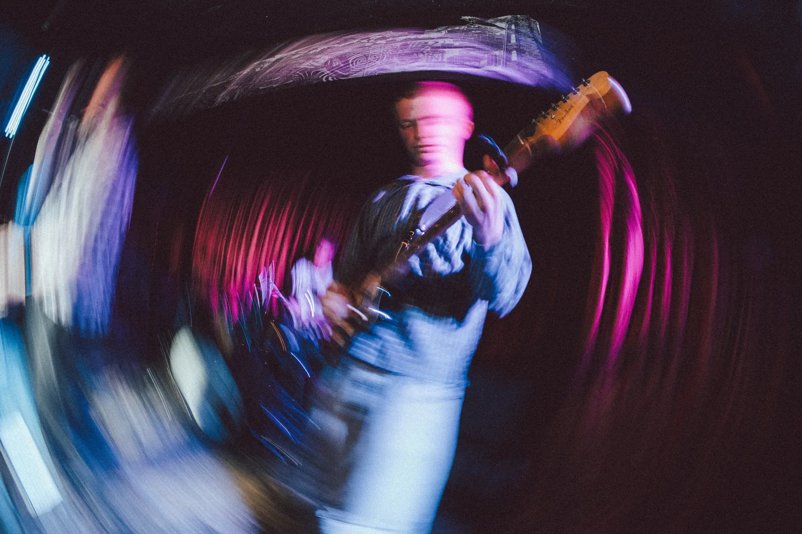 Live music photo of a guitarist with radial motion blur in pink and blue light.