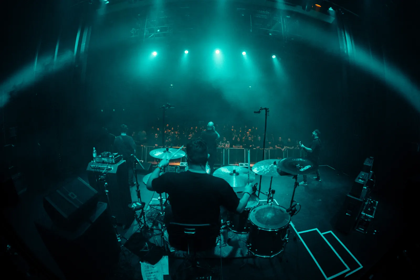 Wide live music photo from behind a drummer on stage.